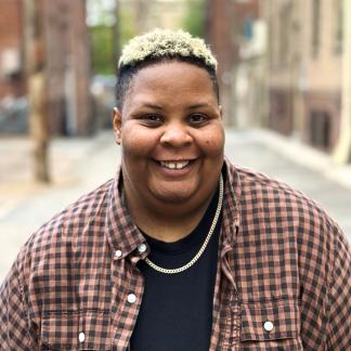 a headshot of shea, wearing a checkered shirt over a black shirt
