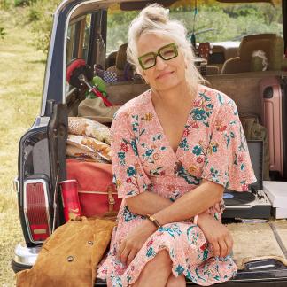 Headshot of Harper Steele, wearing green glasses, a pink floral dress, and sitting in the back of a vehicle