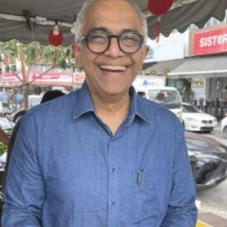 Headshot of Vijayendra Rao wearing a blue button down shirt and black-framed glasses
